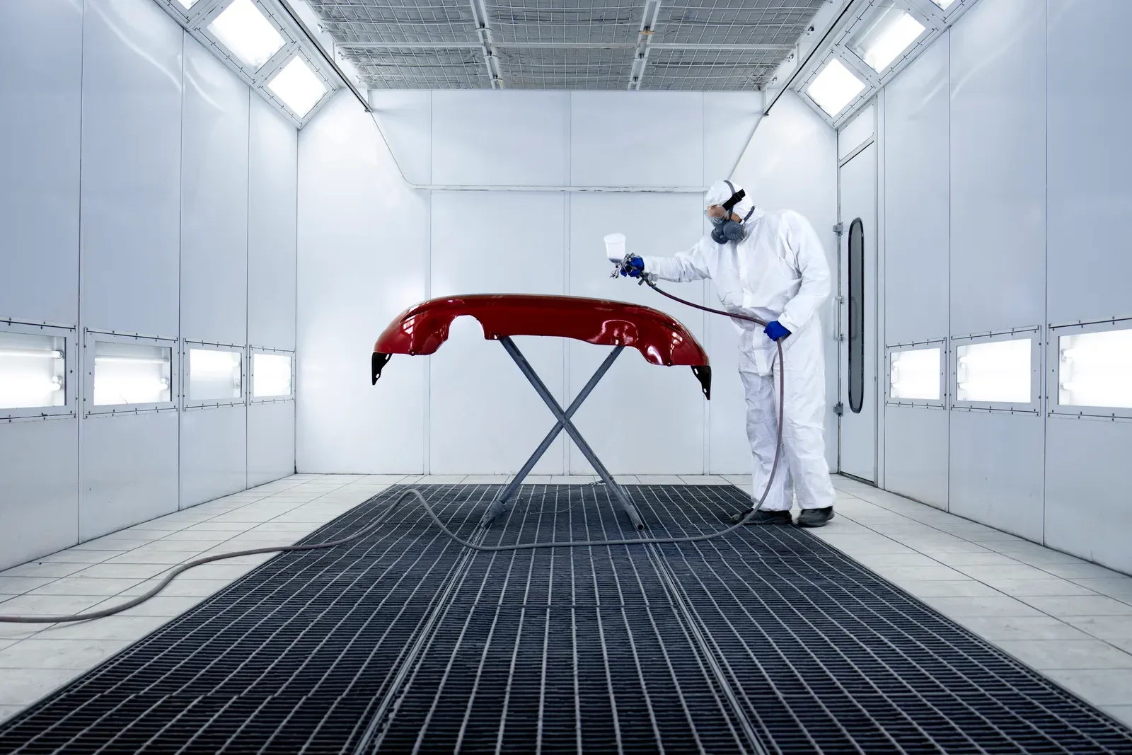 Technician spraying a freshly painted bumper in the paint booth